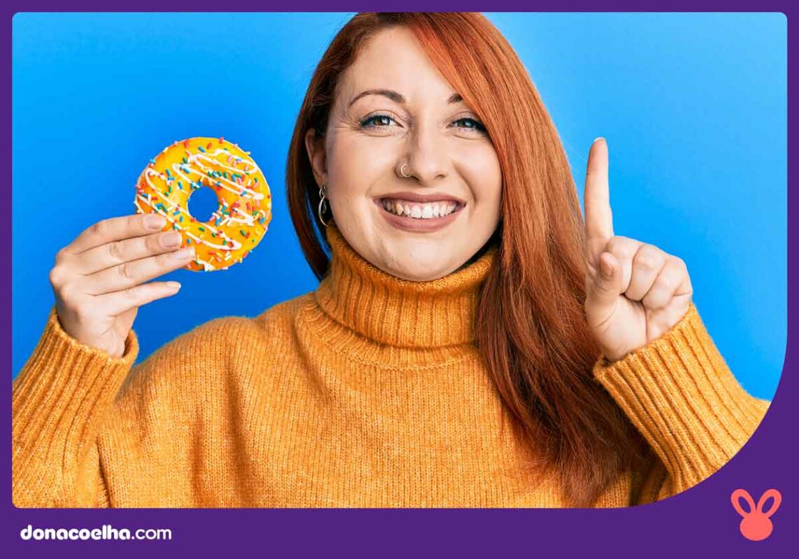 Mulher segurando uma rosquinha e apontando com o dedo da outra mão para cima