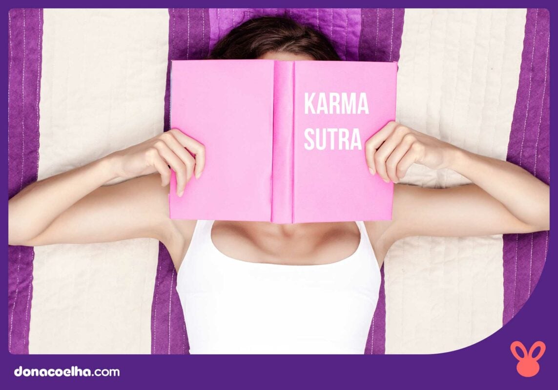 Mulher deitada em uma cama lendo um livro rosa com o título kama sutra