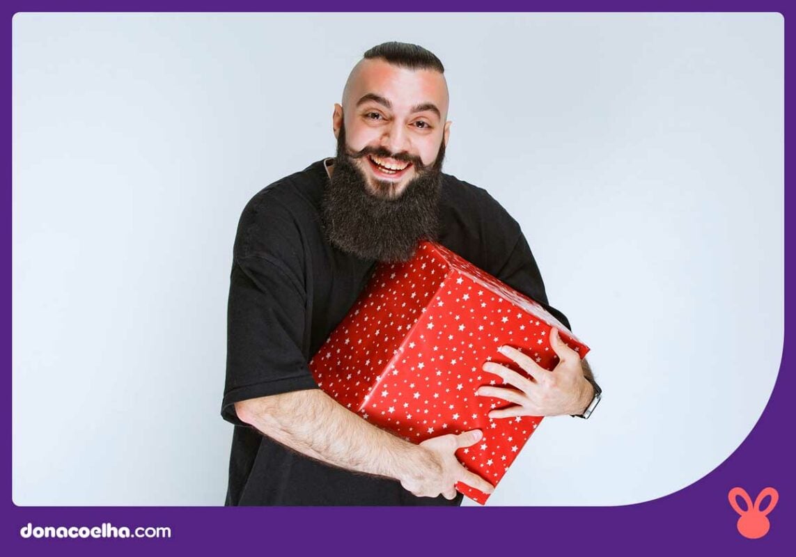 Pessoa de camiseta preta pousando para foto segurando uma grande caixa de presentes