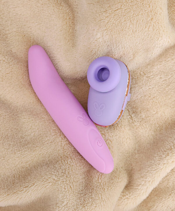 Vibrator rosa e massageador lilás em superfície de plush bege.