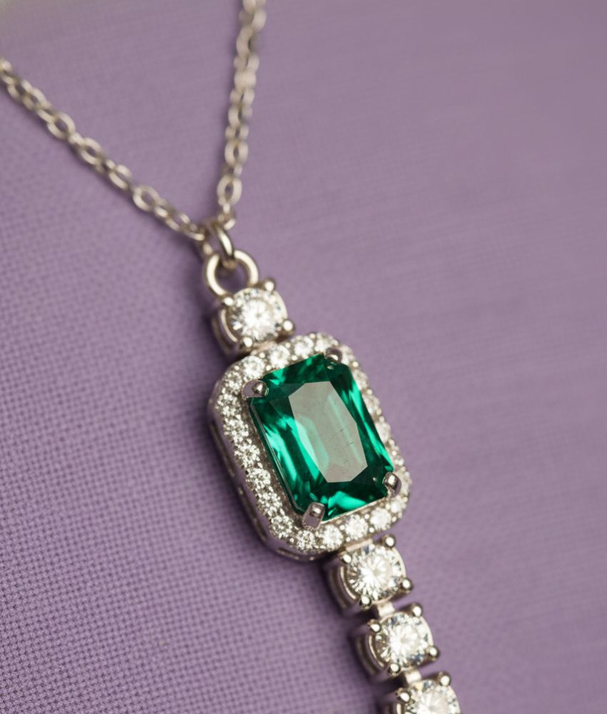 Colar de corrente prateada com pingente de strass verde e detalhes brilhantes.