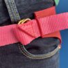 Cinto rosa com detalhes dourados ajustado na cintura de jeans escuros.