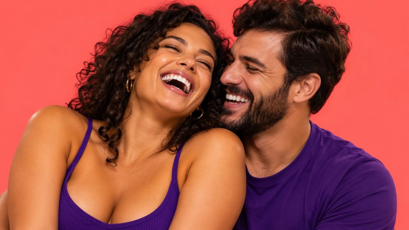 Casal dando uma gargalhada genuína sobre fundo coral, tema insegurança masculina com brinquedo de casal